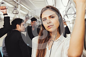 Beautiful young woman passenger standing with headphones and while shirt in the modern subway train