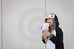 Beautiful, young woman in penguin costume is eating decoration ice cream in front of concrete wall