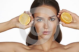 Beautiful young woman with perfect healthy skin and long brown hair day makeup bare shoulders holding orange lemon grapefruit