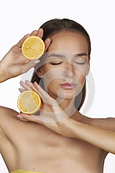Beautiful young woman with perfect healthy skin and long brown hair day makeup bare shoulders holding orange lemon grapefruit