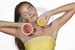 Beautiful young woman with perfect healthy skin and long brown hair day makeup bare shoulders holding orange lemon grapefruit