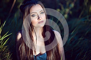 Beautiful young woman with perfect make up and long silky straight hair sitting in the field.