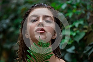 Beautiful young woman with perfect skin and natural make up posing front of plant tropical green leaves background. Teen model