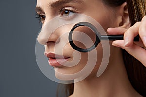 Beautiful young woman with perfect skin using magnifying glass