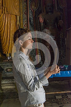 Beautiful young woman performing budhist ritual using incense sticks in the temple