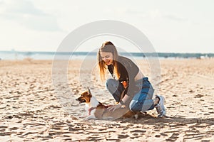 Beautiful young woman petting Corgi puppy, resting on beach. Female walking with dog