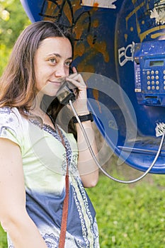 Beautiful young woman in a phone booth. The girl is talking on the phone from the payphone. woman talking by public telephone