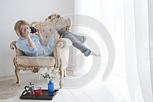 Beautiful young woman with photo camera in big comfortable chair near window