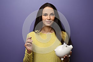 Beautiful young woman with piggy bank and coin on color background