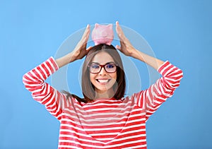 Beautiful young woman with piggy bank on color background