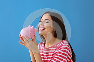 Beautiful young woman with piggy bank on color background