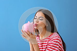 Beautiful young woman with piggy bank on color background