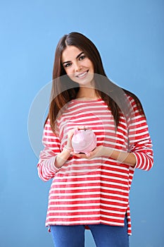 Beautiful young woman with piggy bank on color background