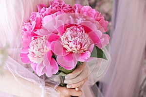 Beautiful young woman in pink dress holding peony flowers bouquet in her hands
