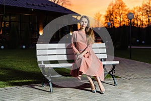 Beautiful young woman in pink dress is sitting on a wooden bench-2.
