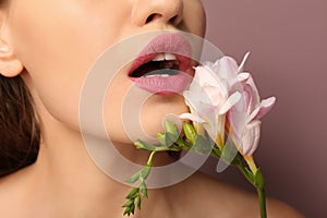 Beautiful young woman with pink lipstick and flower on color background, closeup