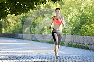 Beautiful young woman in pink top jogging in park