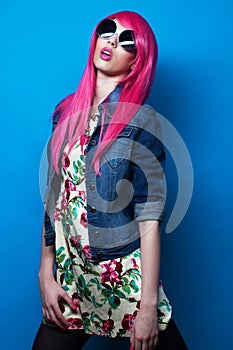 beautiful young woman in pink wig with big sunglasses posing on blue background