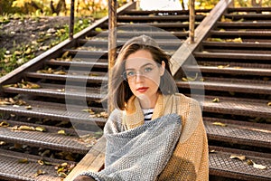 Beautiful young woman with plaid sitting on stairs outdoors