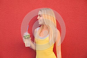 Beautiful young woman with plastic cup of fresh cocktail on color background