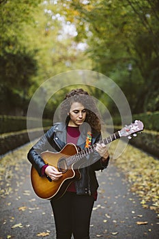 Beautiful young woman playing guitar on forest.