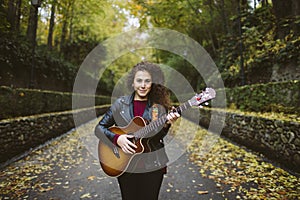 Beautiful young woman playing guitar on forest.