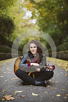 Beautiful young woman playing guitar sitting on the forest.