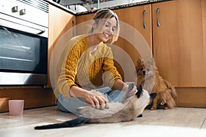 Beautiful young woman playing with her cute lovely animals sitting on the floor in the kitchen at home