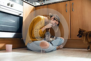 Beautiful young woman playing with her cute lovely animals sitting on the floor in the kitchen at home