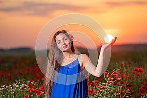 Beautiful young woman playing with sun ball while standing in poppy field in warm sunset light