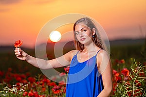 beautiful young woman playing with sun ball while standing in poppy field in warm sunset light