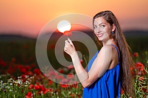 Beautiful young woman playing with sun ball while standing in poppy field in warm sunset light