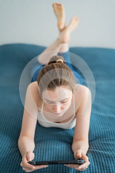 A beautiful young woman plays in Nintendo Switch lying on the bed. Videogame controller