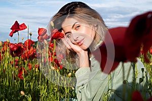 Beautiful young woman in poppy field. Woman on flowering poppy field. Summer holidays on nature. Girl on poppies meadow