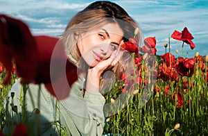 Beautiful young woman in poppy field. Woman on flowering poppy field. Summer holidays on nature. Girl on poppies meadow