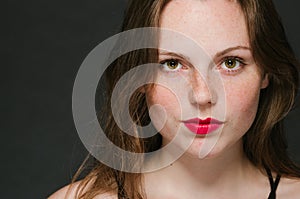 Beautiful young woman portrait on black background studio with red lips and freckles