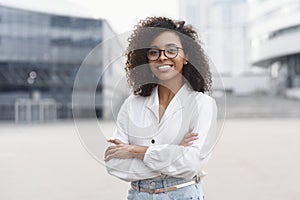 Beautiful young woman portrait in a city. Smiling african american girl with crossed arms looking at camera.