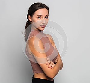 Beautiful young woman portrait with crossed arms. Successful woman looking at camera isolated on gray, copy space for text. Studio