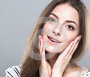 Beautiful young woman portrait cute tender pure smiling touching her cheeks by fingers attractive gray background