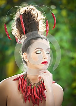 Beautiful young woman portrait with red hot spicy peppers around the neck and in hair, fashion model with creative food vegetable