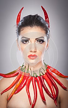 Beautiful young woman portrait with red hot and spicy peppers, fashion model with creative food vegetable make up