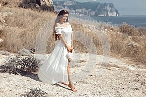 Beautiful young woman portrait in a white dress with woven handbag enjoying in the hay field. Natural beauty female. Romantic