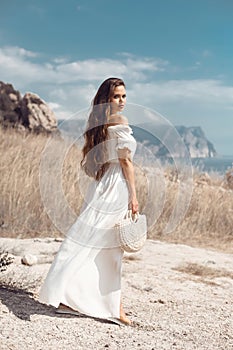 Beautiful young woman portrait in a white dress with woven handbag enjoying in the hay field. Natural beauty female. Romantic