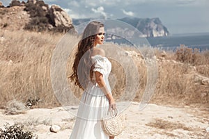 Beautiful young woman portrait in a white dress with woven handbag enjoying in the hay field. Natural beauty female. Romantic