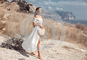 Beautiful young woman portrait in a white dress with woven handbag enjoying in the hay field. Natural beauty female. Romantic