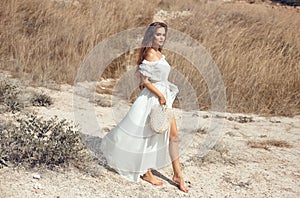Beautiful young woman portrait in a white dress with woven handbag enjoying in the hay field. Natural beauty female. Romantic