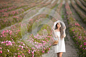 Beautiful young woman portrait in white hat over roses field. Carefree happy brunette with healthy wavy hair having fun outdoor in