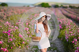 Beautiful young woman portrait in white hat over roses field. Carefree happy brunette with healthy wavy hair having fun outdoor in