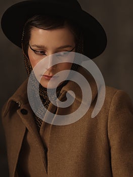 A beautiful young woman poses in the studio on a gray background. Vintage look. Autumn or spring coat, black hat and
