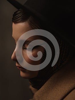 A beautiful young woman poses in the studio on a gray background. Vintage look. Autumn or spring coat, black hat and